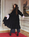 Calf-length black coat with wide smocking in premium quality cotton. The blue lining is made of a mixture of cotton and silk.